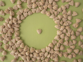 Extruded heart-shaped bran is poured onto a green background forming a circular void space for the...