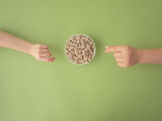 Extruded heart-shaped bran in a white bowl on a green background, children's hands reach for the...