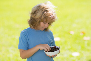 Summer child. Funny kid eats cherries. Excited face. Cherry for kids. Teenager child hold plate cherries. Healthy food.