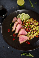 Sliced Organic grilled Tuna fillet covered with sesame seeds and salsa on black ceramic plate