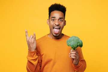 Young cool man wear orange sweatshirt casual clothes hold broccoli do horns up gesture isolated on...