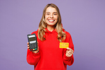 Young woman wears red hoody casual clothes hold wireless modern bank payment terminal process acquire credit card isolated on plain pastel light purple background studio portrait. Lifestyle concept.