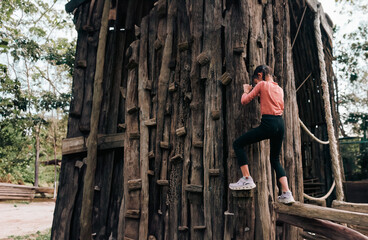 Unidentified little girl is climbing on wooden wall in the natural playground. Concept of outdoor playing for kid development, brave, risk, security, freedom,active lifestyle.
