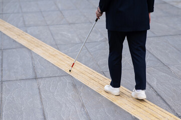 Close-up of the legs of a blind businesswoman walking along a tactile tile with a cane. 