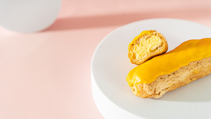 Eclair with mango custard cutaway and yellow icing on pastel pink background. Delicious eclair with cream filling covered with yellow melted glaze. Close up. Cafe menu, confectionery special offer