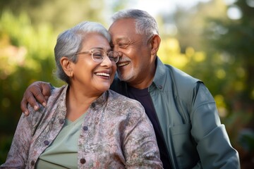 Fototapeta premium Elderly partners, both in their late 70s, South Asian, cuddling affectionately against a soft green pastel background