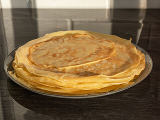 Close-up shot of a plate with thin, golden pancakes in sunlight on a grey table