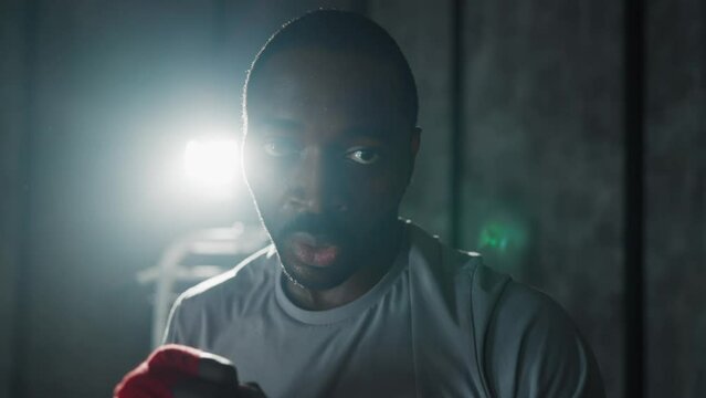 Portrait aggressive man boxer in gym. African american sportive focused sweated fighter during boxing training, break looking at camera. Workout, strength fight professional sport, box concept.