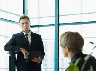 selective focus businessman in suit standing with tablet in relaxing workplace while looking at collegue man. colleague men working in modern office