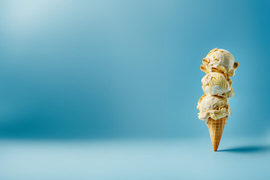 glace, cr&egrave;me glac&eacute;e,  3 boules parfum banane caramel, avec des morceaux de fruits, sur un cornet en gaufre, sur un fond bleu clair avec espace n&eacute;gatif pour texte, copyspace 