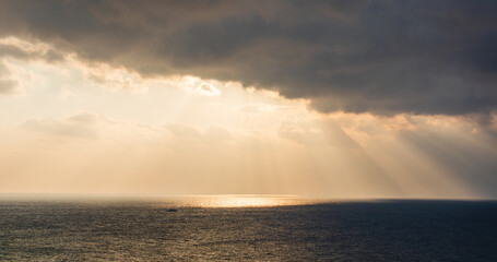 Obraz premium Majestic ocean sunrise scenery with sunlight shining through dark clouds