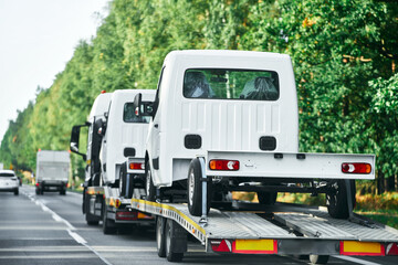 Fototapeta na wymiar Emergency towing service in action on the highway. A yellow tow truck transports a damaged car on a flatbed carrier. The rear view of the vehicles shows the brake lights and the motion of the traffic.