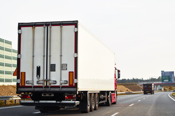 Semitrailer trucks transporting cargo on the highway. The trucks are delivering goods by land from door to door. They are part of a global sustainable logistics industry that supports trade commerce
