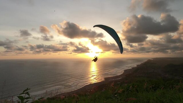 The paraglider is flying over the beach with a beautiful sunset and clouds in the background