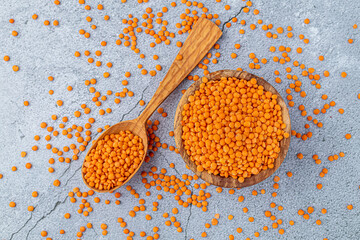 Photo of red lentils in wooden bowl with wooden measuring cup on wooden background.  Healthy lifestyle. Vegetarian and vegan diet.