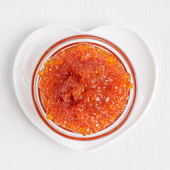 Top view of heap of salted red caviar or salmon fish roe served in glass bowl on heart shaped plate on white wooden table used as ingredient for healthy holiday appetizers or snacks full of protein