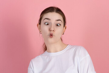 Portrait of attractive Caucasian young brunette woman with funny face wearing casual white t-shirt isolated on pink studio background.