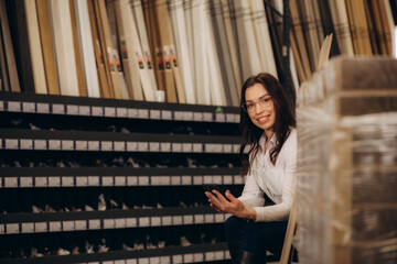 Happy brunette female interior designer choosing flooring tile color texture samples at store shop. Woman architect choice floor and wall finishing material for architecture and construction industry