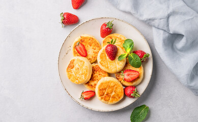 Cottage cheese, cheesecakes or syrniki with strawberries and mint leaves on a white plate on a light background with napkin. The concept of a nutritious and healthy breakfast. Top view and copy space.