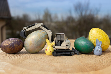 model of a toy gray excavator and multi-colored Easter eggs on a wooden stump. Easter spring...