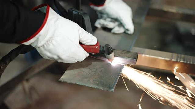 Heated metal plate surface being cut with oxy fuel torch in workshop, sparks and flame in the process of cutting, welder in protective gloves dividing steel on parts, metalwork and manufacturing