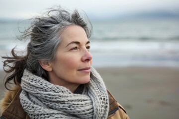 Middle-aged woman with first gray hair smiling on beach, sea in background - 742440949