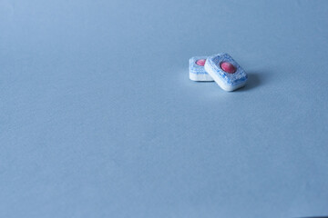 Two blue dishwasher tablets on a blue background with space for text.