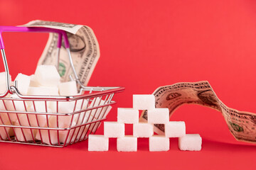Shopping basket with sugar cubes and paper money bills on a red background. Selective focus. Copy space.
