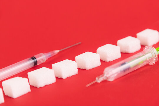 White sugar cubes and insulin syringe on a red background. Copy space.