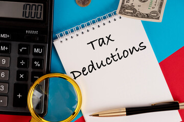 Tax deductions, the text is written in a white notepad, next to a calculator, a pen and a magnifying glass.
