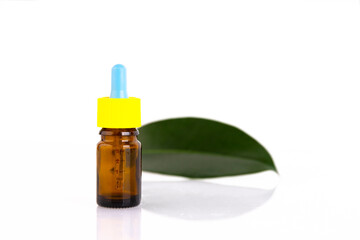 Blank amber glass essential oil bottle with pipette on green leaves background. Copy space