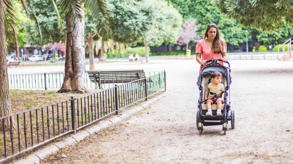 Woman strolls through a park lifting a stroller with her child