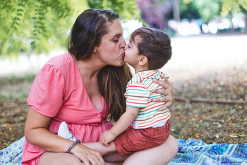 A mother gives her son a kiss sitting in a park