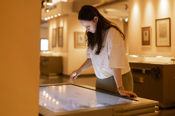 Getting information via touchscreen, young woman using touch screen at university or museum
