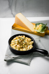 a skillet of macaroni and cheese with a slice of cheese on a cutting board