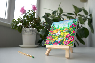 A picture of a Ukrainian village with an wooden easel lies on the background of a vase. Decorative art. Petrykivka painting still life.