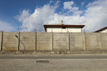 Long precast concrete wall with barbed wire on top. Sidewalk and street in front, blue cloudy sky...