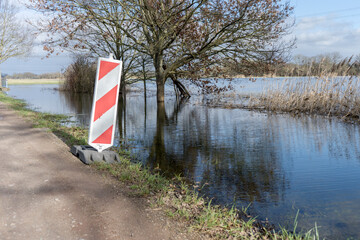 Road next to flooded meadows with warning bark