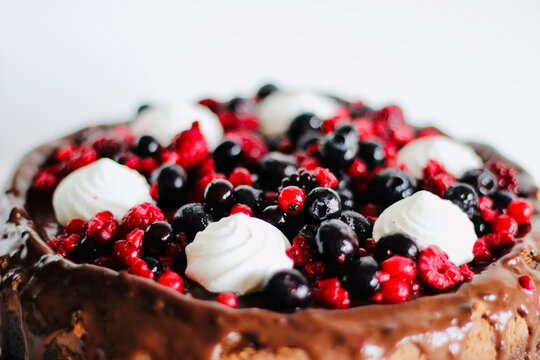 Close-up of homemade chocolate cheesecake with fresh raspberries, blueberries and redcurrants with whipped cream