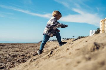 The boy jumps up on the sandy beach near the sea. a 3-year-old boy in a checkered shirt plays on...
