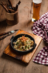 a pan of risotto with peas and asparagus on a wooden table next to a glass of beer
