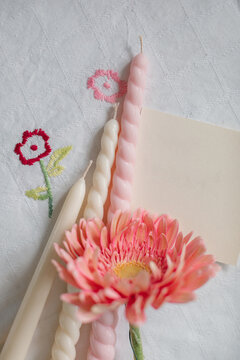 Overhead view of assorted candles, blank paper card and gerbera flowers on a floral tablecloth