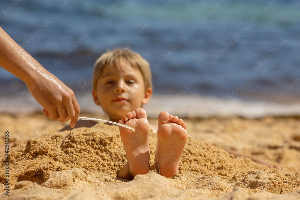 Sticker Child, tickling sibling on the beach on the feet with feather, kid cover in sand, smiling, laughing