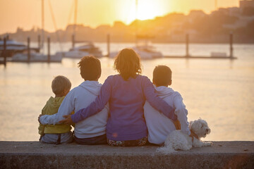 Children, boys, brothers, enjoying sunset over river with their pet maltese dog and mom, boats, sun, river - obrazy, fototapety, plakaty