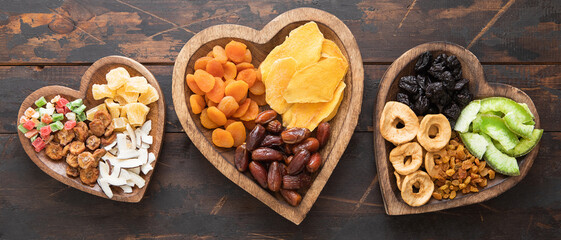 Healthy sweet dried fruits and berries in wooden heart shaped plates on wooden background.Top view. - Powered by Adobe