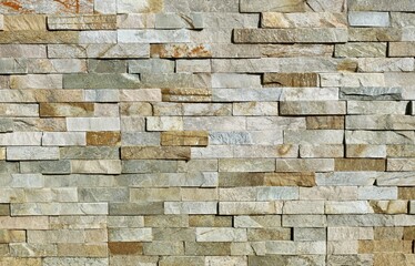 Stone cladding wall made of striped stacked bricks of  rocks. Main colors are brown, gray, green and white. Extternal wall covering, background and texture.	