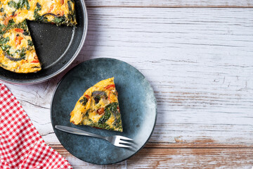 Italian Frittata made with spinach, tomatoes, onion and peppers on white wooden table. Top view. Copy space
