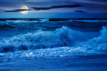 waves crashing the shore of black sea at night. stormy seascape in full moon light