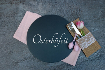 Text Osterbüfett auf einer Schieferplatte geschrieben mit Besteck Blumen und Ostereiern.