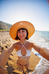 The girl takes a selfie. Close-up of a cheerful young girl in a summer hat taking a selfie on the beach.